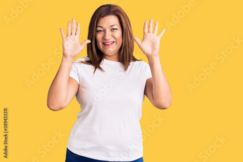 Middle age latin woman wearing casual white tshirt showing and pointing up with fingers number ten while smiling confident and happy.