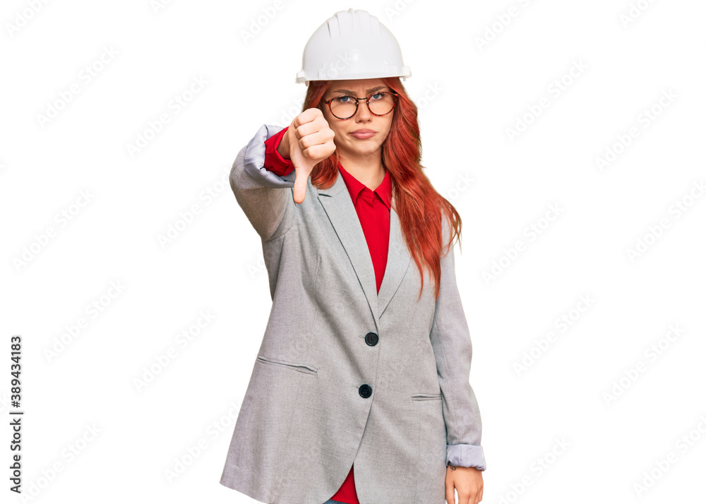 Young redhead woman wearing architect hardhat looking unhappy and angry showing rejection and negative with thumbs down gesture. bad expression.