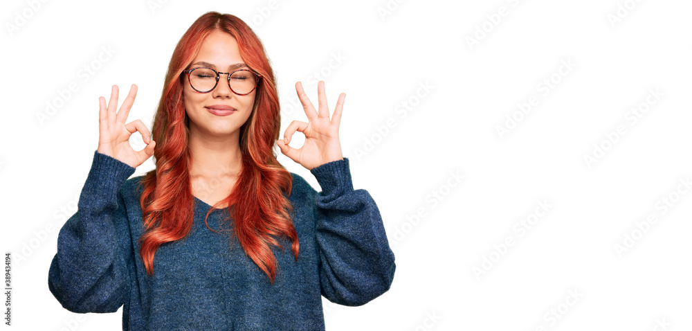 Young redhead woman wearing casual sweater and glasses relax and smiling with eyes closed doing meditation gesture with fingers. yoga concept. Young redhead woman wearing casual sweater and glasses relax and smiling with eyes closed doing meditation gesture with fingers. yoga concept.