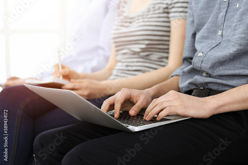 Group of casual dressed business people working at meeting or conference in sunny office, close-up of hands. Businessman using laptop computer