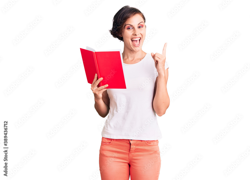 Beautiful young woman with short hair reading a book surprised with an idea or question pointing finger with happy face, number one Beautiful young woman with short hair reading a book surprised with an idea or question pointing finger with happy face, number one