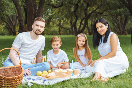 Portrait of a happy family hugging and looking at the camera while relaxing on the lawn during a picnic in a green garden