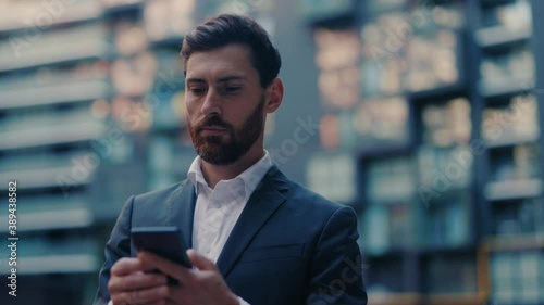 Adult successful caucasian serious businessman in formal outfit walking in corporate business district with phone browsing financial news smartphone application. photo