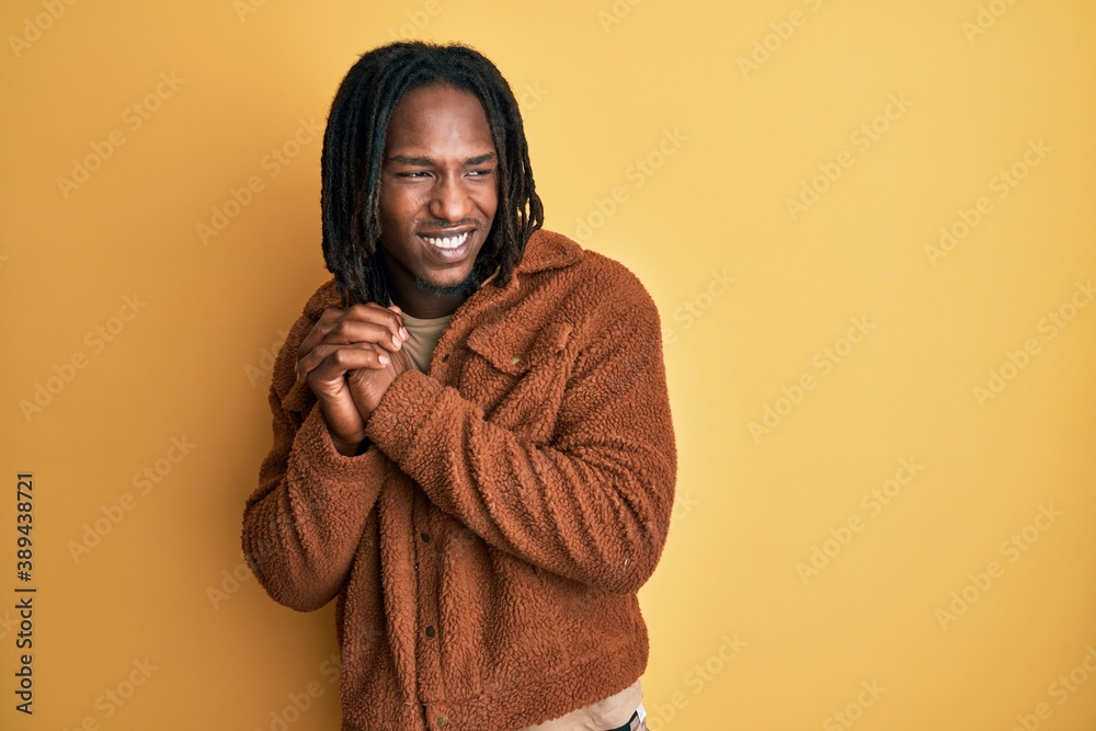 African american man with braids wearing brown retro jacket laughing nervous and excited with hands on chin looking to the side African american man with braids wearing brown retro jacket laughing nervous and excited with hands on chin looking to the side