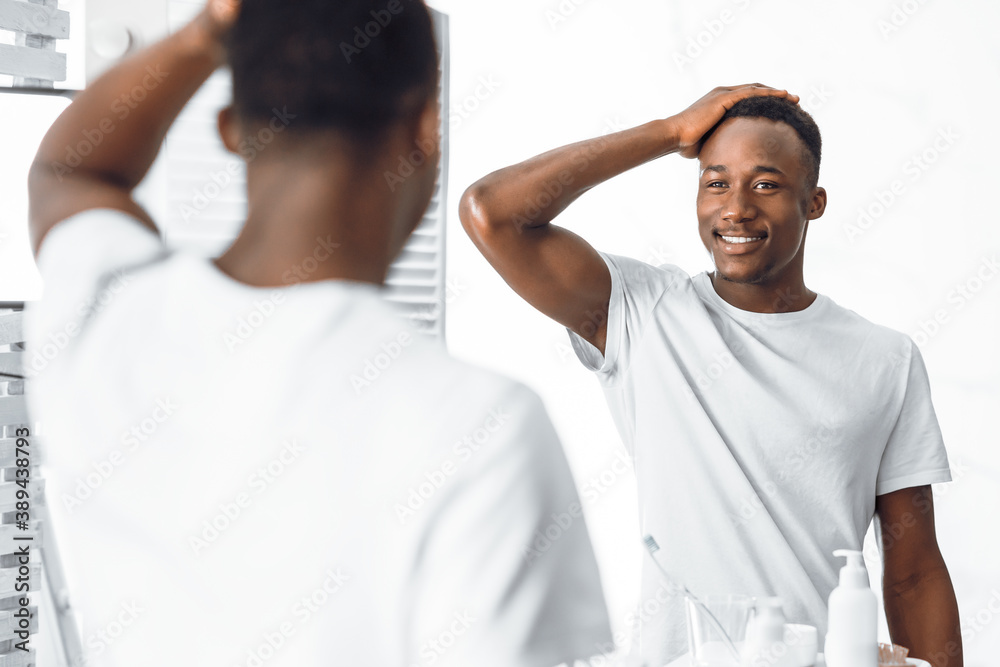African American Guy Touching Hair Looking In Mirror In Bathroom African American Guy Touching Hair Looking In Mirror In Bathroom
