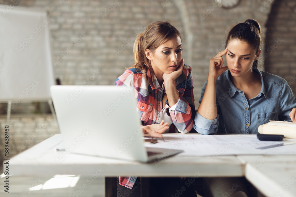 Frustrated businesswomen having problems while working on blueprints in the office Frustrated businesswomen having problems while working on blueprints in the office