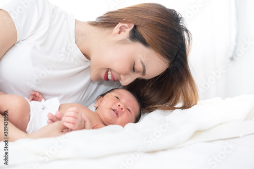 Beautiful asian women mother long hair in the white pajamas. mom kiss at newborn infant with love, while a baby sleeping in her arm with warm, safe, comforted resting on the clean bed. © sutlafk