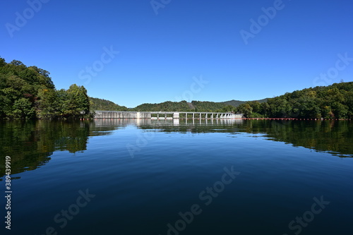 Santeetlah Dam on Lake Santeetlah and Cheoah River in Graham County, North Carolina reflected in calm water of lake on clear autumn afternoon.