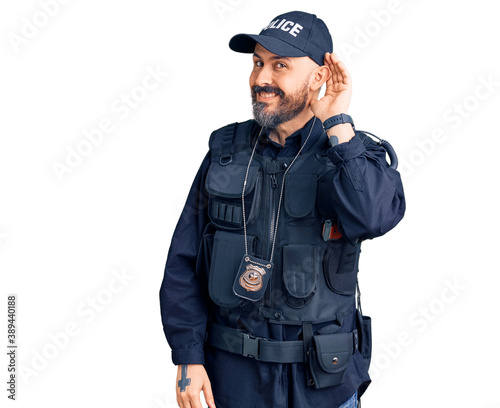 Young handsome man wearing police uniform smiling with hand over ear listening an hearing to rumor or gossip. deafness concept.