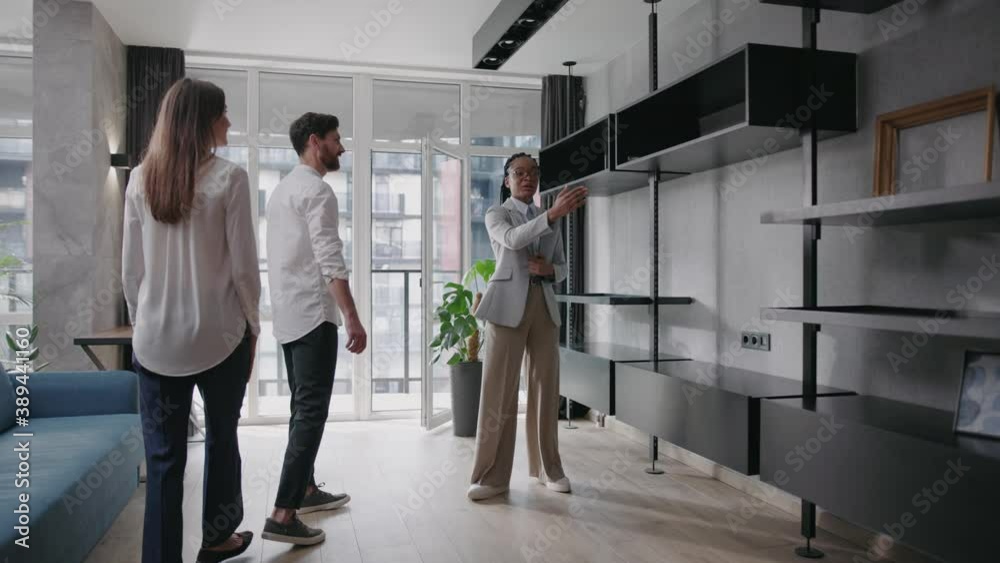 African american female real estate agent showing luxury modern apartment to young happy caucasian family buying new house. Realtor. Accommodation. Deals.