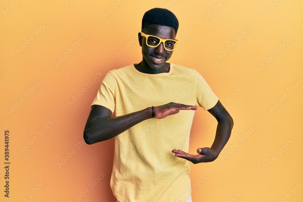 Young african american man wearing casual clothes and glasses gesturing with hands showing big and large size sign, measure symbol. smiling looking at the camera. measuring concept.