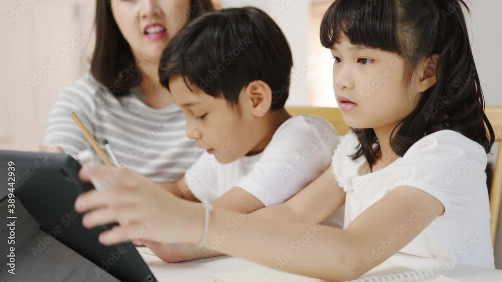 Happy Asia family homeschooling, mother teach children using digital tablet in living room at home. Spending time together, Self-isolation, Social distancing, Quarantine for corona virus prevention. Happy Asia family homeschooling, mother teach children using digital tablet in living room at home. Spending time together, Self-isolation, Social distancing, Quarantine for corona virus prevention.