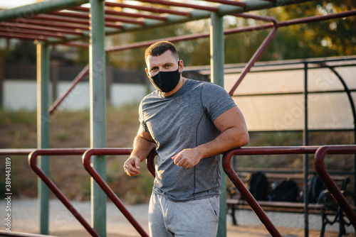 A young man does push-UPS, pull-UPS on a sports field in a mask during a pandemic at sunset. Sports, healthy lifestyle © Andrii