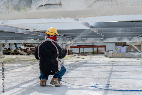 The painter is working to fireproof paint on steel structure with spray gun, at industrial factory.