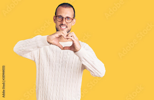 Young handsome man wearing casual clothes and glasses smiling in love doing heart symbol shape with hands. romantic concept.