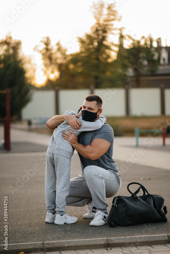 A father and child stand on a sports field in masks after training during sunset