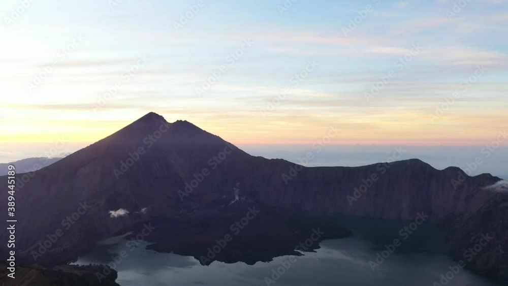 Cinematic aerial downwards reveal of Rinjani Lake and summit at predawn, thus a colourful sky. Lombok Island, Indonesia. Cinematic aerial downwards reveal of Rinjani Lake and summit at predawn, thus a colourful sky. Lombok Island, Indonesia.