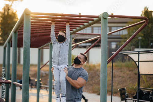 Father and son play sports on the sports field in masks during sunset. Healthy parenting and healthy lifestyle