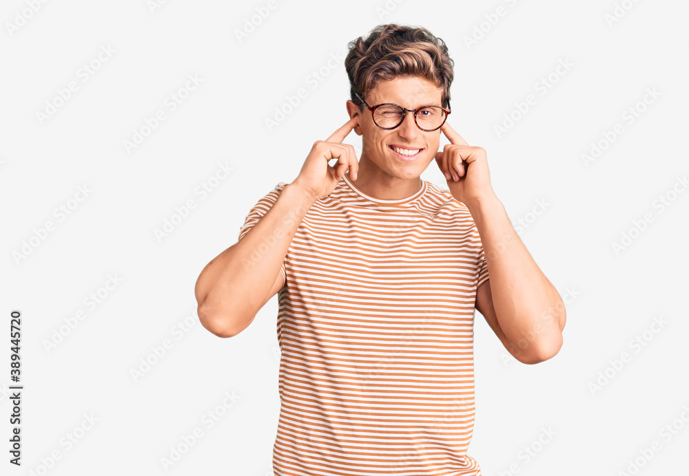 Young handsome man wearing casual clothes and glasses covering ears with fingers with annoyed expression for the noise of loud music. deaf concept. Young handsome man wearing casual clothes and glasses covering ears with fingers with annoyed expression for the noise of loud music. deaf concept.