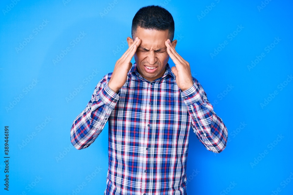 Young handsome latin man wearing casual clothes with hand on head for pain in head because stress. suffering migraine. Young handsome latin man wearing casual clothes with hand on head for pain in head because stress. suffering migraine.
