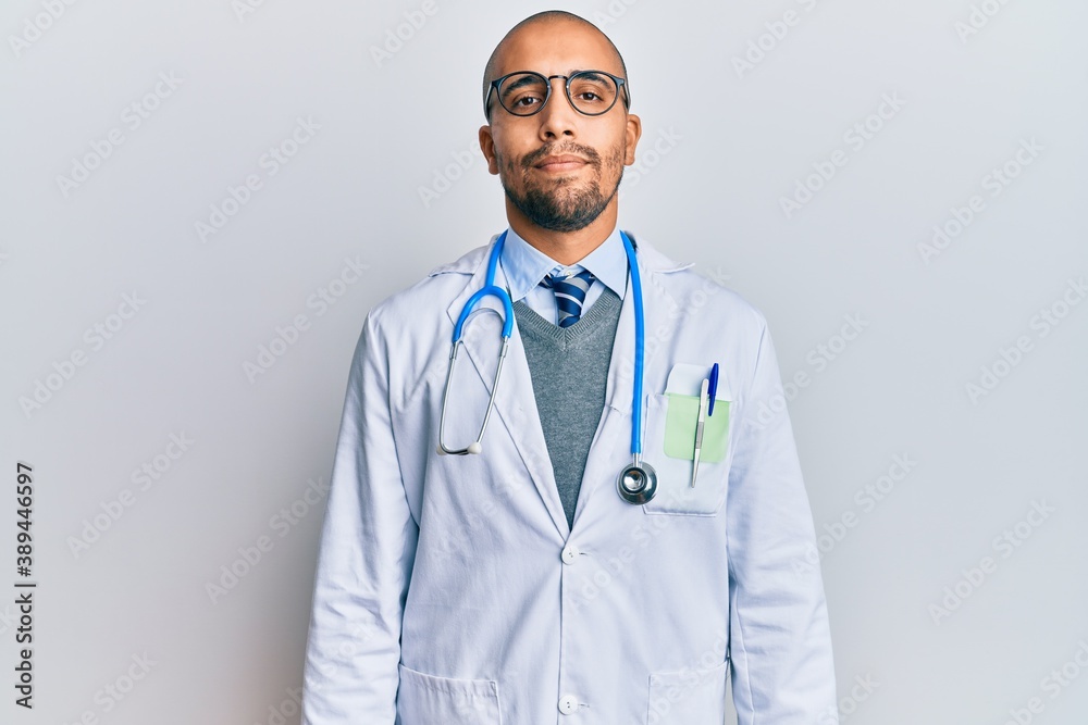 Hispanic adult man wearing doctor uniform and stethoscope relaxed with serious expression on face. simple and natural looking at the camera. Hispanic adult man wearing doctor uniform and stethoscope relaxed with serious expression on face. simple and natural looking at the camera.