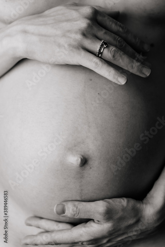 Hands on the naked belly of a pregnant woman. Black and white vertical close up.