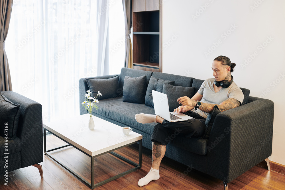 Handosme fit man sitting on sofa at home and answering e-mail or programming on laptop Handosme fit man sitting on sofa at home and answering e-mail or programming on laptop