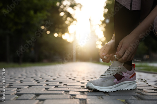 Woman tying shoelaces before morning run in park, closeup. Space for text