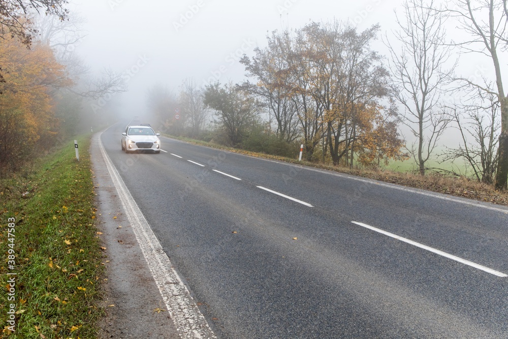 Fototapeta premium Cars in the fog. Bad autumn weather and dangerous automobile traffic on the road. Light vehicles in fog. Slippery road. Dangerous driving.