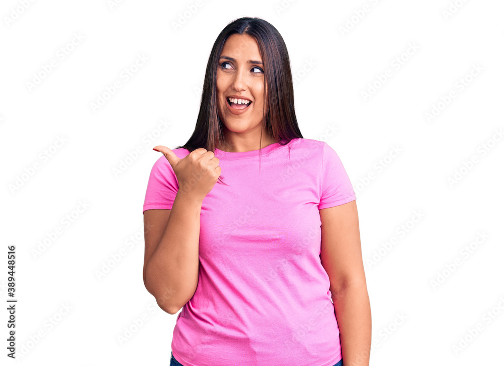 Fototapeta premium Young beautiful brunette woman wearing casual t-shirt smiling with happy face looking and pointing to the side with thumb up.