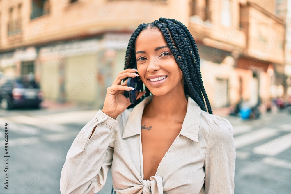 Fototapeta premium Young african american woman smiling happy talking on the smartphone at the city.