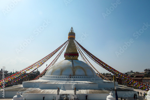 A panoramic view at the Boudhanath Temple in Kathmandu  Nepal. Golden face of Buddha shines bright. Many prayer flags surrounding the top. Bright blue sky. Wisdom eyes.