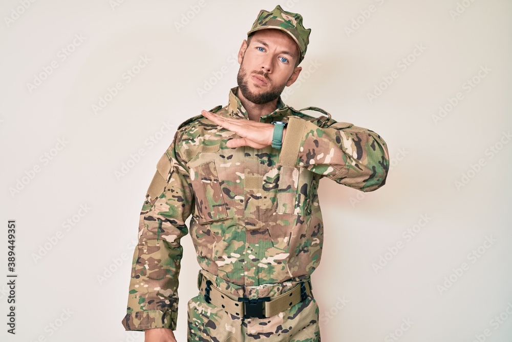Young caucasian man wearing camouflage army uniform cutting throat with hand as knife, threaten aggression with furious violence Young caucasian man wearing camouflage army uniform cutting throat with hand as knife, threaten aggression with furious violence