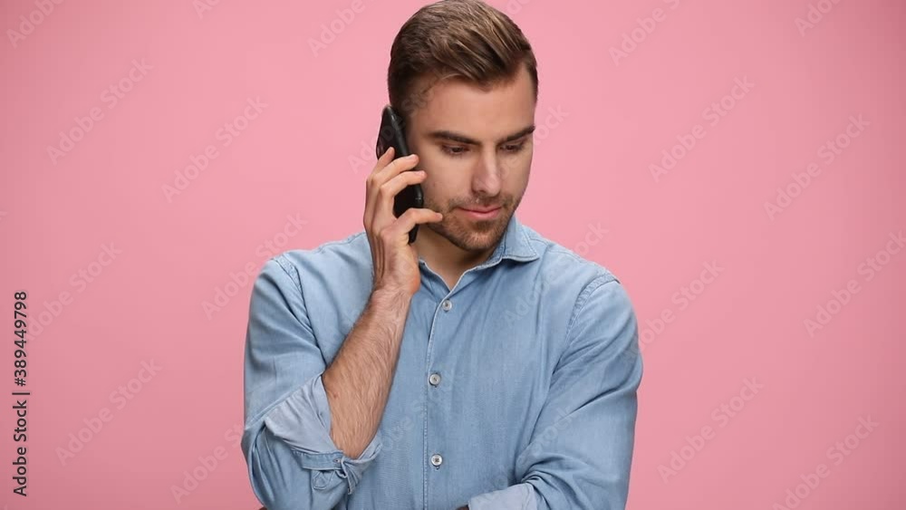 smiling young casual man in denim shirt talking on the phone, holding fist in the air and cheering on pink background smiling young casual man in denim shirt talking on the phone, holding fist in the air and cheering on pink background