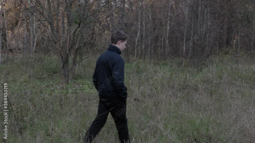 A teenager in a black jacket walks through the woods near an old ruined building. High quality 4k footage A teenager in a black jacket walks through the woods near an old ruined building. High quality 4k footage