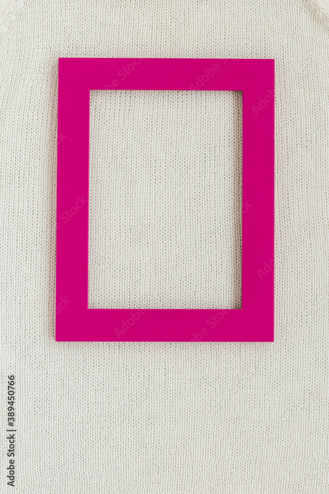 Bright pink color frame lying on white knitted fabric with mockup of template at bright light view from above. Concept of fashion and advertisement background.