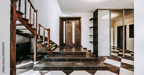 Modern interior of entrance hall in luxury apartment. Wooden door and staircase. Tile floor. Wardrobe. Private house.