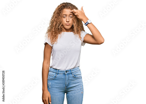Beautiful caucasian teenager girl wearing casual white tshirt pointing unhappy to pimple on forehead, ugly infection of blackhead. acne and skin problem