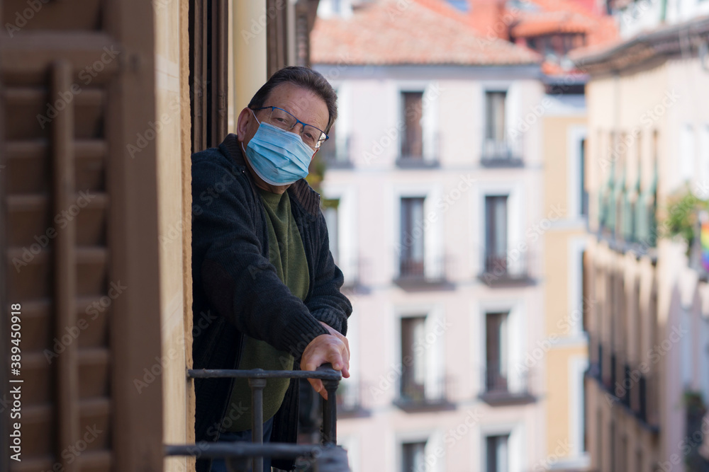 mature man in balcony home lockdown during covid19 outbreak - senior male on his 70s in face mask worried and tired looking to the street thoughtful and depressed in quarantine