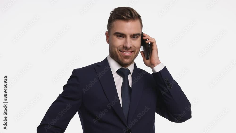 smiling young man in navy blue suit talking on the phone and pointing fingers, standing isolated on white background in studio smiling young man in navy blue suit talking on the phone and pointing fingers, standing isolated on white background in studio
