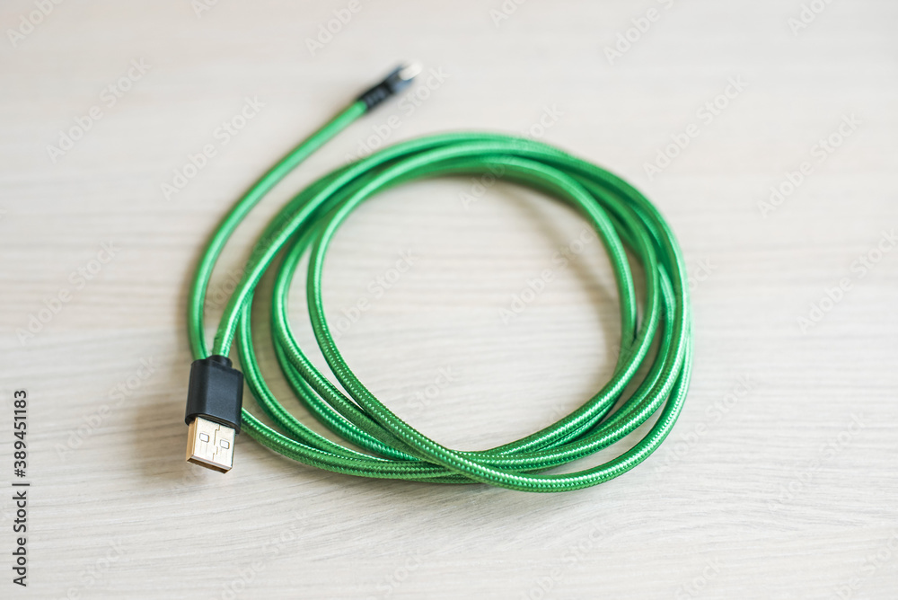 Contemporary coiled usb cable with green covering case lying on textured wooden table at bright light extreme close view. Electric connection equipment. Contemporary coiled usb cable with green covering case lying on textured wooden table at bright light extreme close view. Electric connection equipment.