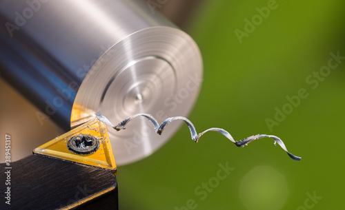 Beautiful spiral metal swarf. Close-up of turning on green background. Detail of lathe tool bit with yellow triangle carbide insert when working dural cylindric workpiece. Twisted alu chip. Machining.