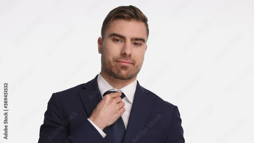 attractive young man in navy blue suit fixing tie, seductively smiling and crossing arms, looking down and rising eyebrows, standing isolated on white background in studio attractive young man in navy blue suit fixing tie, seductively smiling and crossing arms, looking down and rising eyebrows, standing isolated on white background in studio