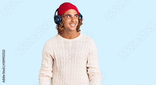 Young hispanic man listening to music using headphones smiling looking to the side and staring away thinking.