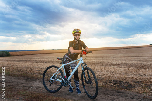 smiling girl standing with a bicycle in the middle of the evening field