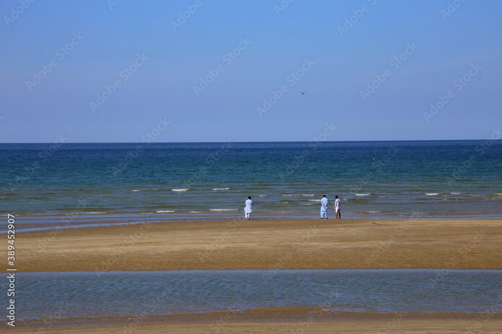Three people standing on the shore, between the beach and the sea Three people standing on the shore, between the beach and the sea