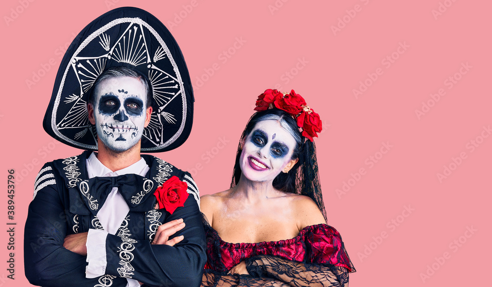 Fototapeta premium Young couple wearing mexican day of the dead costume over background happy face smiling with crossed arms looking at the camera. positive person.