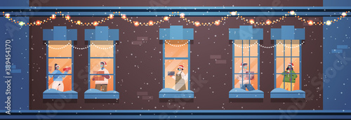people in santa hats holding gifts mix race neighbors standing in window frames new year christmas holidays celebration self isolation concept building house facade horizontal vector illustration