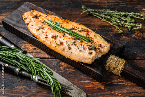 Baked trout fillet on a cutting board. Dark wooden background. Top view