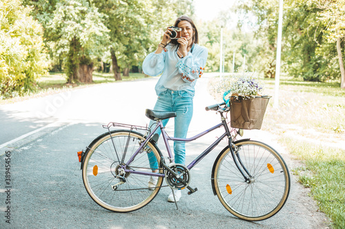 A stylish woman standing near a bicycle while using a retro camera.